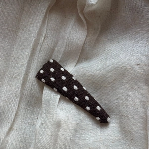 Close-up of brown knitted triangle BB clip with white polka dots on linen fabric