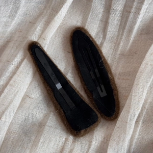 Detail view of two dark brown fuzzy hair clips on beige fabric for autumn and winter styles