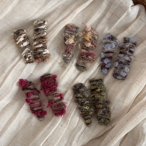 Five pairs of handmade gradient yarn hair clips in autumn colors on a soft white background