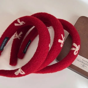 Detailed close-up of red knitted headband with embroidered bows and handmade label detail