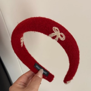 Detail of red knitted headband showing white bow embroidery and handmade woven label