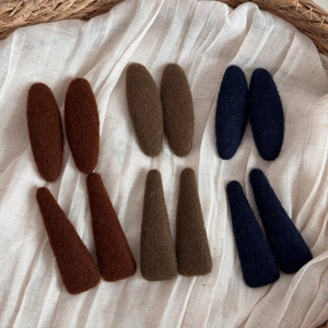 Close-up of wool felt hair clips in earthy tones displayed on textured linen fabric