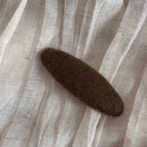 Close-up of a coffee brown wool felt teardrop hair clip on a natural linen background