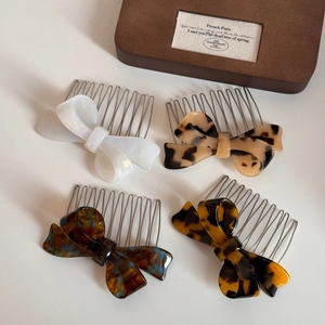 Detail view of four elegant acetate bow hair combs in white, yellow, and tortoiseshell patterns