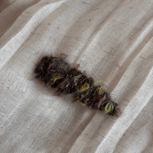 Close-up of mixed brown and yellow wool hair clip on natural beige linen background