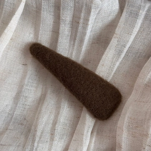 Detailed view of coffee brown felt hair clip on a minimalist beige linen background