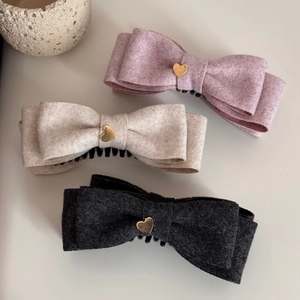 Dettaglio di fermagli a fiocco in rosa, beige e grigio con ciondoli a cuore oro