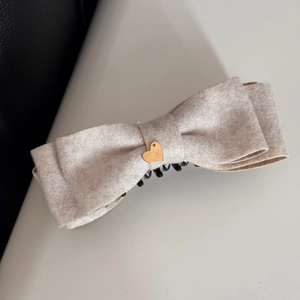 Dettaglio della molletta per capelli con fiocco in tweed beige e ciondolo a cuore dorato