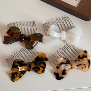 Detail view of acetate bow hair side combs in marble, pearl white, and tortoiseshell patterns