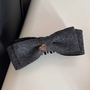 Dettaglio di un fermaglio per capelli a fiocco in feltro grigio scuro con ciondolo a cuore d'oro
