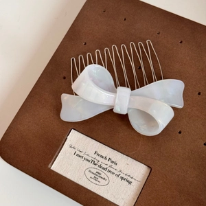 Detail of pearlescent bow hair comb with nine silver metal teeth on a display card