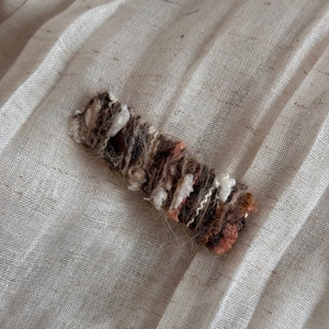 Close-up of a hand-knitted rectangular hair clip with warm-toned gradient wool yarn textures