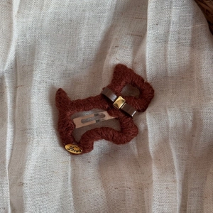 Detail einer handgestrickten Hundespange aus braunem Garn mit goldenem Love-Anhänger