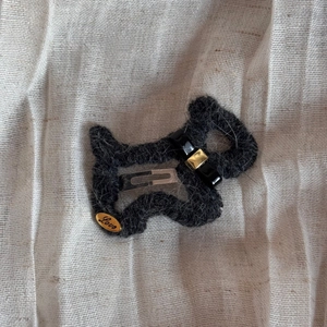 Detail der schwarzen gestrickten Welpen-Haarspange mit goldenem Anhänger und Metallclip