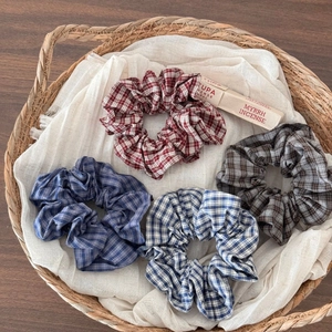 Close-up of four plaid scrunchies in red, blue, and brown displayed in a woven basket
