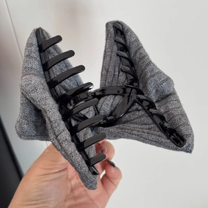 Detail view of large grey knitted bow hair claw clip with multi-tooth black inner grip