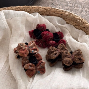 Close-up of three tweed bow hair clips in red and brown showing woven fabric textures