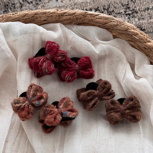Detailed close-up of handmade knit bow hair clips in autumn colors on linen texture