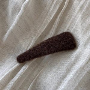 Detail of dark brown wool felt BB hair clip on minimalist beige linen background
