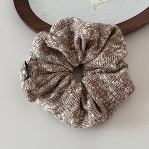 Close-up of brown and white knit scrunchie with detailed woven texture and brand label