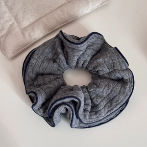 Detailed texture of dark grey knitted scrunchie with navy blue trim on white desk