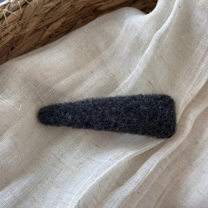 Detailed texture of dark grey felt BB hair clip on a soft natural linen background