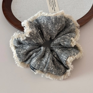 Detailed close-up of knitted scrunchie texture with cream tassels and fashion label
