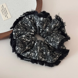 Detail of a large black and white tweed scrunchie with fringe edges and fashion label