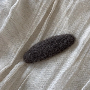 Close-up of a charcoal grey felt hair clip on a soft white linen fabric background