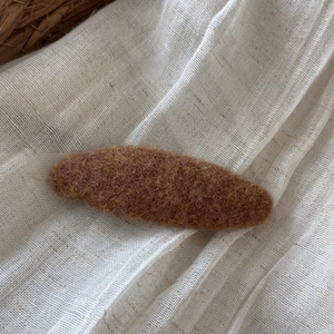 Detail view of oval brown felt hair clip on white fabric with natural rustic elements