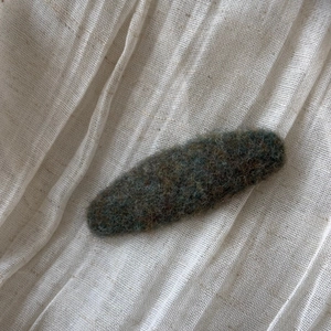 Detailed close-up of dark green felt fabric hair clip texture on white linen background