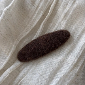 Detailed view of dark brown felt fabric hair clip on a natural linen background
