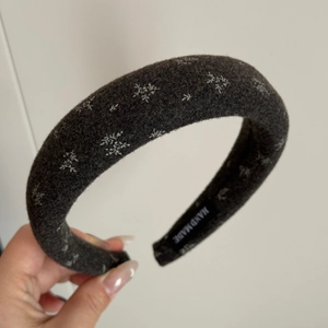 Detailed view of dark grey wool headband with white snowflake embroidery and handmade tag
