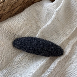 Close-up of a charcoal gray felt oval hair clip on textured beige linen fabric