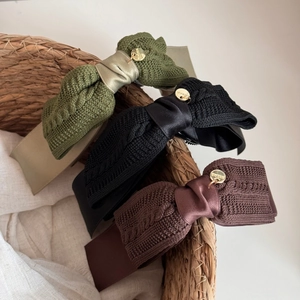 Detail of cable knit bow hair clips in green, black, and red with gold metal brand emblems