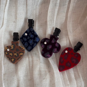 Detailed macro view of four poker-shaped hair clips with flocked leopard print and small rhinestones
