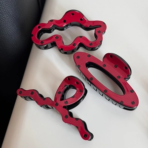 Detailed view of three red and black polka dot hair claws in various elegant shapes