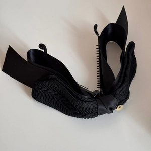 Close-up of black satin bow banana clip showing gold emblem and non-slip inner teeth