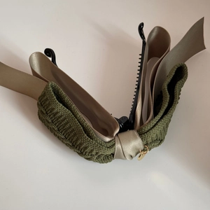 Detail of banana hair clip with green knit bow, champagne ribbons, and gold pendant