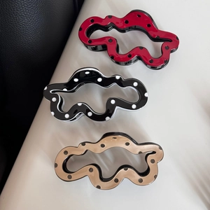 Detailed view of wave-shaped polka dot hair claws in red, black, and champagne gold