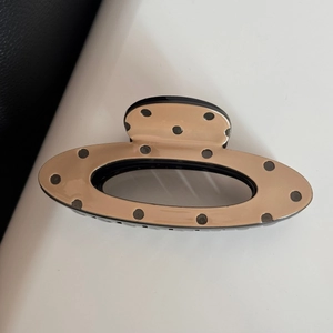 Close-up of beige polka dot hair claw clip with black teeth on a textured background