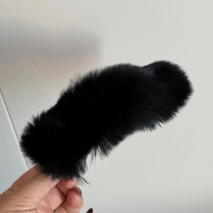 Gros plan d'une pince à cheveux en fausse fourrure noire tenue à la main sur fond blanc