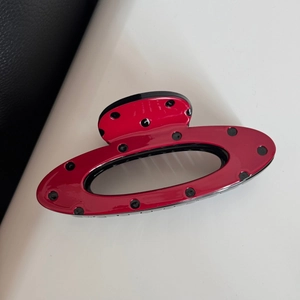 Detailed view of a red polka dot hair claw clip with black rivets and a hollow oval design