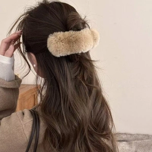 Détail d'une pince à cheveux en fourrure de vison kaki portée sur de longs cheveux ondulés