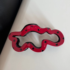 Close-up of wavy red shark hair clip with black polka dots on a minimalist split background