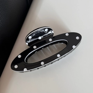 Close-up of black and white polka dot hair claw clip with glossy finish and oval hollow design