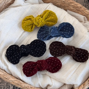 Close-up of five colorful velvet polka dot bow hair clips in a rustic wicker basket