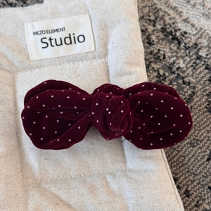 Macro detail of wine red velvet polka dot bow hair clip on a textured linen surface