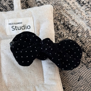 Detail of a black velvet polka dot bow hair clip placed on a beige linen jewelry pouch