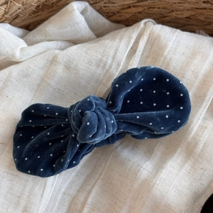 Close-up of navy velvet polka dot bow hair clip on a natural woven basket background